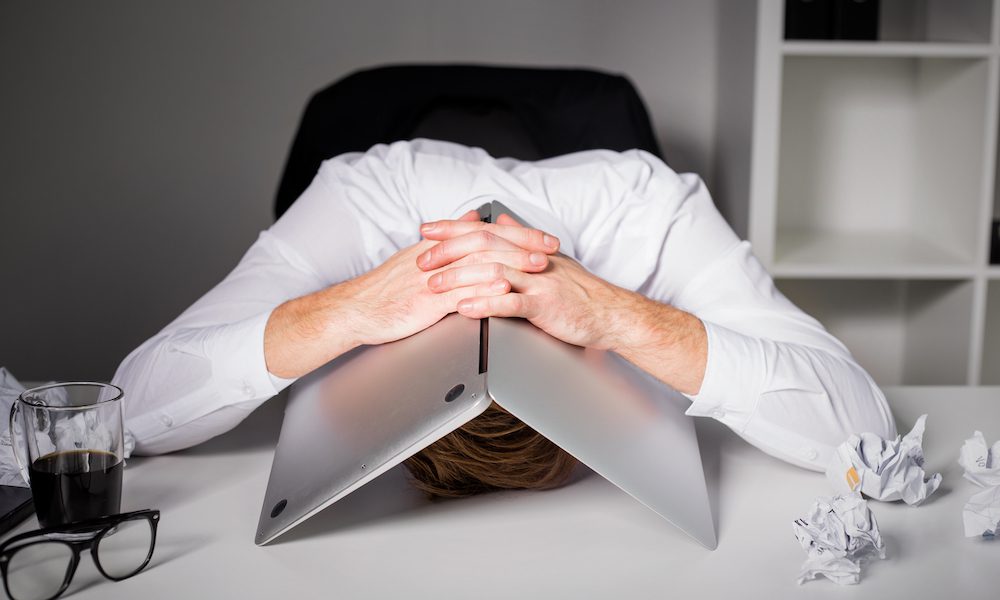 Avoiding Wage and Hour Violations - Man Tired and Frustrated With Head Under Laptop