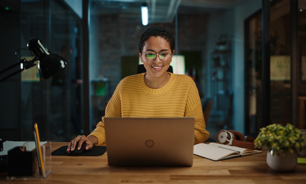 Portrait of Young Latina Marketing Specialist Working on Laptop Computer in Busy Creative Office Environment. Beautiful Diverse Multiethnic Female Project Manager is Browsing Internet.