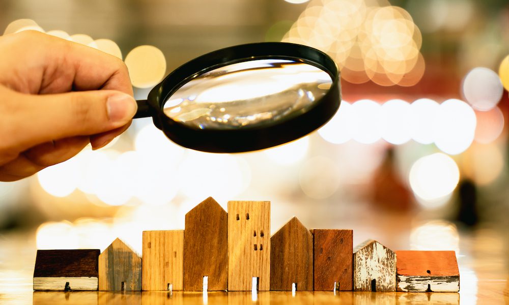 Hand holding magnifying glass and looking at house model, house selection, real estate concept.